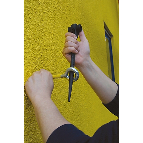 Hände halten Werkzeug zur Wandmontage. Gelbe Wand im Hintergrund, Fenster. Werkzeug: Schwarz, Gelb und Silber.